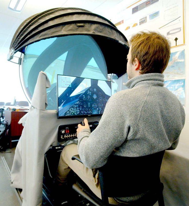 A man sits in front of a flight simulator in an aerospace training lab A man sits in front of a flight simulator in an aerospace training lab