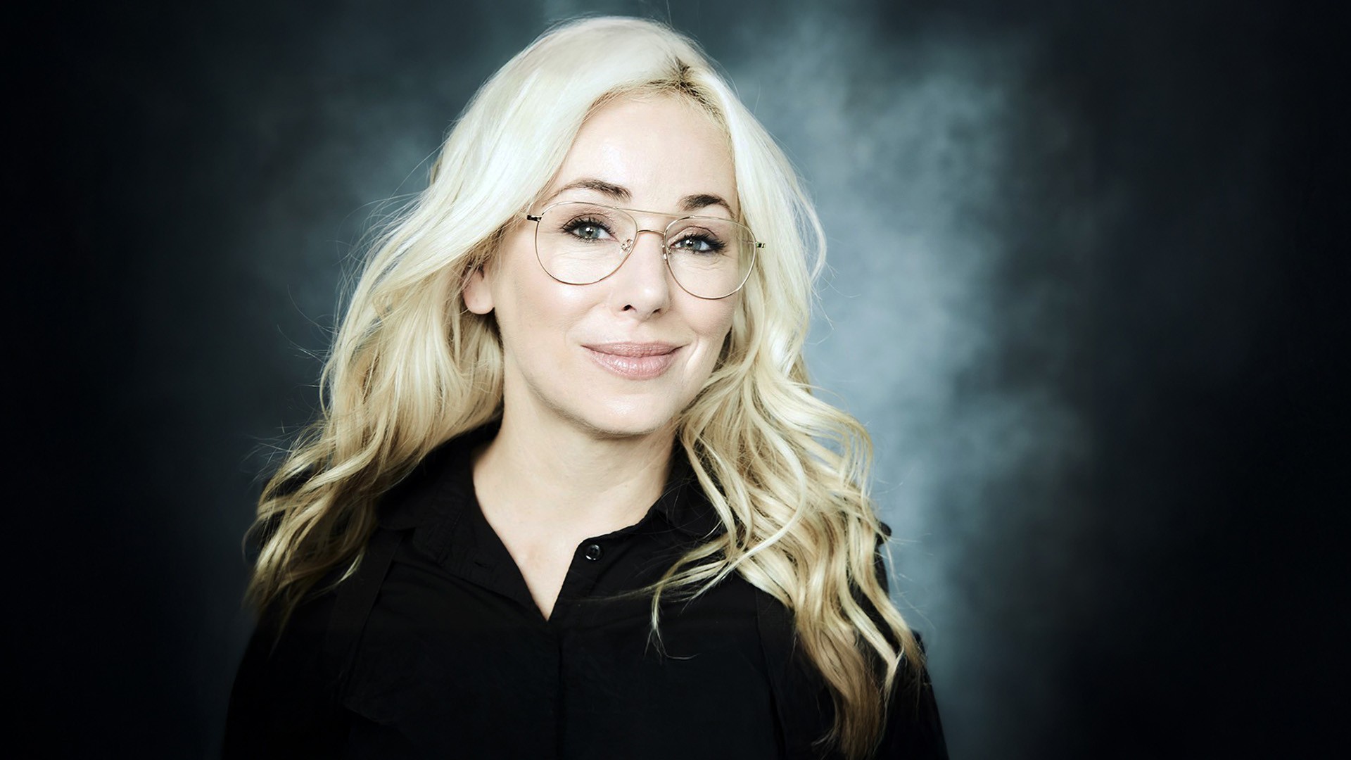 Mariloup has long blonde hair and wears aviator gold-rim glasses.