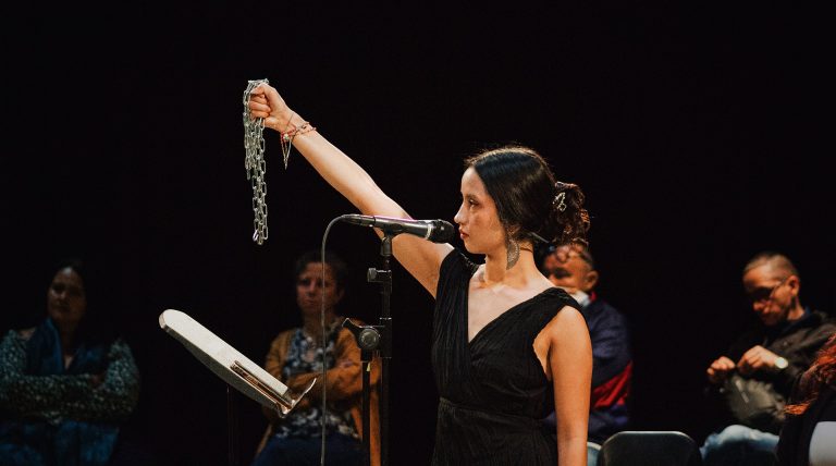 A young woman with long, black hair, wearing a black sleeveless dress and holding up a silver chain.